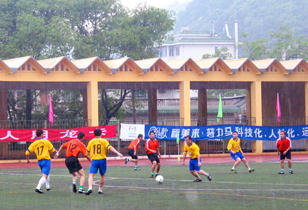 图为首场比赛两队队员冒雨在球场上拼抢。