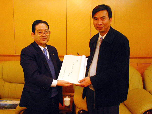 梁宏校长请李刚寿先生(左)将其亲笔签名的书转赠予池田大作先生。
